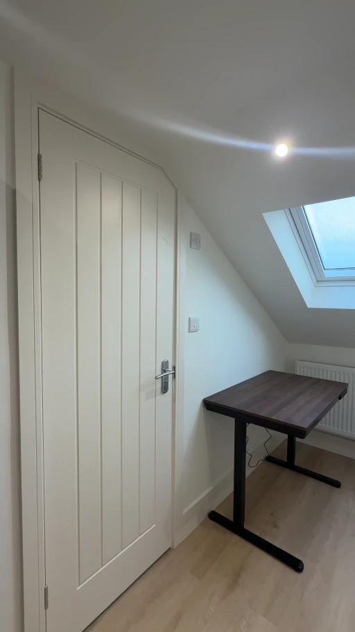 A finished loft interior with freshly painted pale walls, white panelled door and skylight
